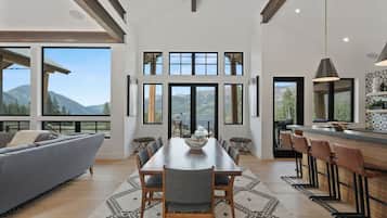 A modern kitchen with a dining area, large windows, and a view of mountains.