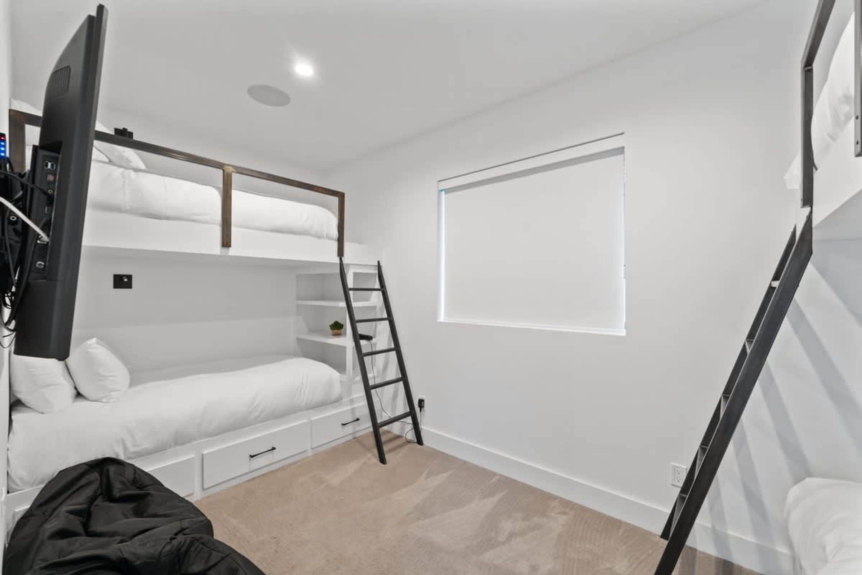 A bunk bed room with a ladder, a window, and a TV.