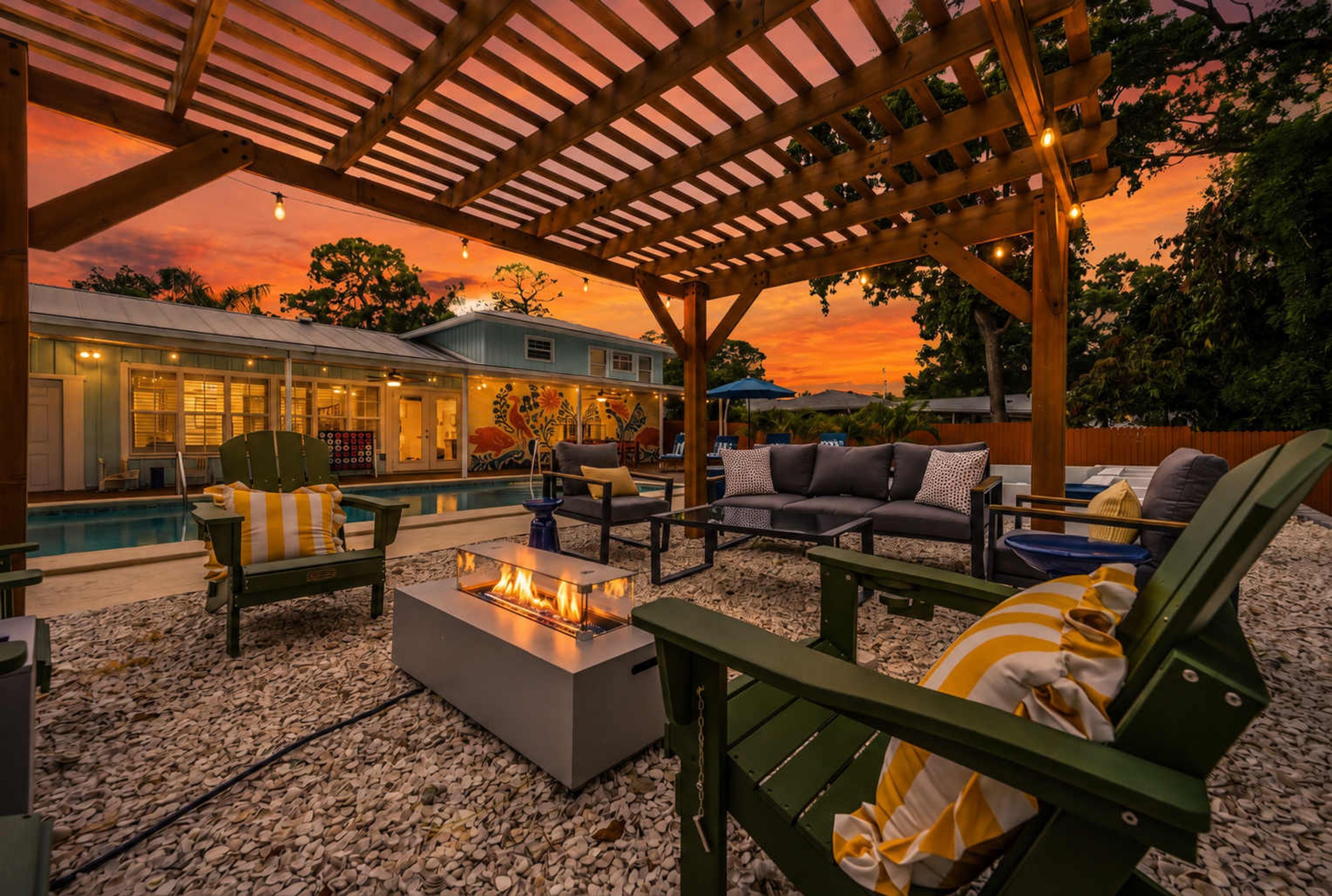 A covered outdoor seating area with a pool, lounge chairs, and a fire feature.