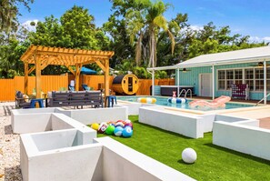 Un jardin avec une pergola en bois, une piscine et un petit bâtiment.