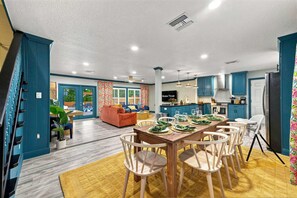 Une cuisine moderne avec des meubles bleus, un coin repas avec des chaises en bois et un salon avec un canapé et vue sur la piscine.