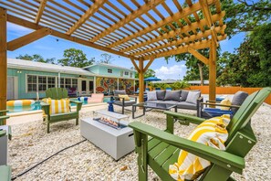 Eine Außenpatio mit Holz-Pergola, Liegestühlen, einem Pool und einer Feuerstelle.