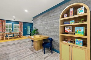 Ein Kinderspielbereich mit einer hölzernen Bücherwand, einem Schachbrett und einem blauen Sessel.