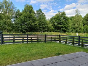 Een geplaveid gebied met een houten omheining, gras en bomen op de achtergrond.