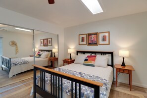 Quarto de hotel com uma cama grande, duas mesas de cabeceira, um criado-mudo, um espelho e uma janela com vista.