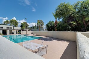 Piscina com mesa e cadeiras, cercada por um muro baixo e árvores.