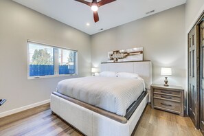 A bedroom with a large bed, a nightstand, a dresser, a ceiling fan, and a window with a view of trees.