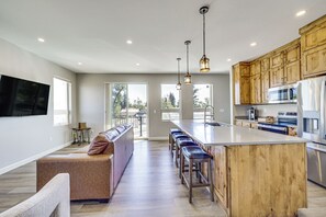 A modern kitchen with a central island, bar stools, wooden cabinets, and a large window.