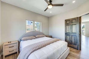A bedroom with a bed, a nightstand, a ceiling fan, a window, and a door.
