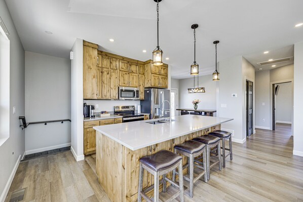 A modern kitchen with wooden cabinets, stainless steel appliances, a large island with bar stools, and pendant lighting.