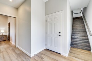 Um corredor com porta branca, piso de madeira e escada com degraus de madeira.