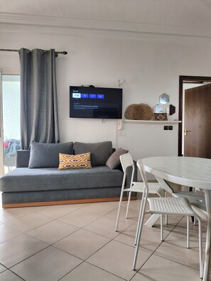 A living room with a grey sofa, a TV mounted on the wall, a white table, and a door.