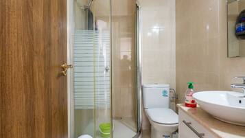 A bathroom with a glass shower enclosure, a toilet, and a sink.