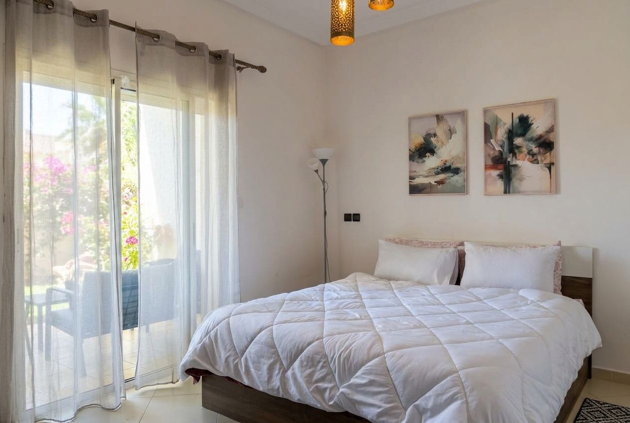 A bedroom with a bed, a floor lamp, and two paintings on the wall.