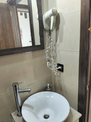 A bathroom with a white sink, a hairdryer mounted on the wall, and a mirror.