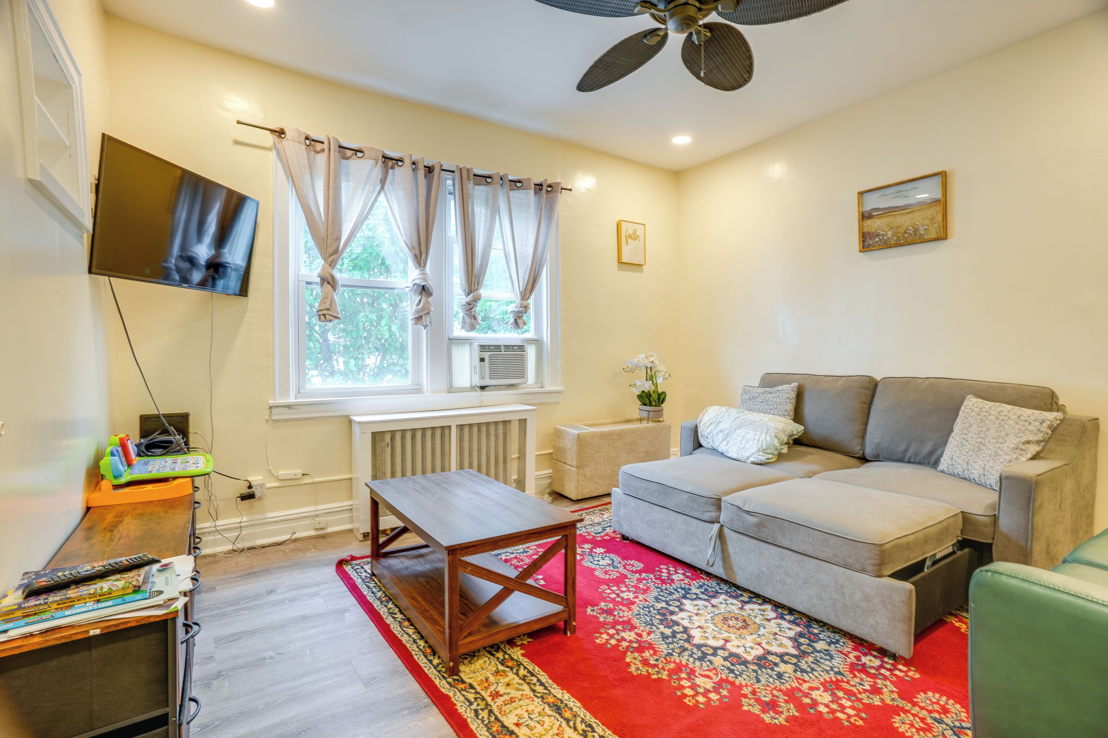 A living room with a sofa, a TV, a ceiling fan, and a window with curtains.