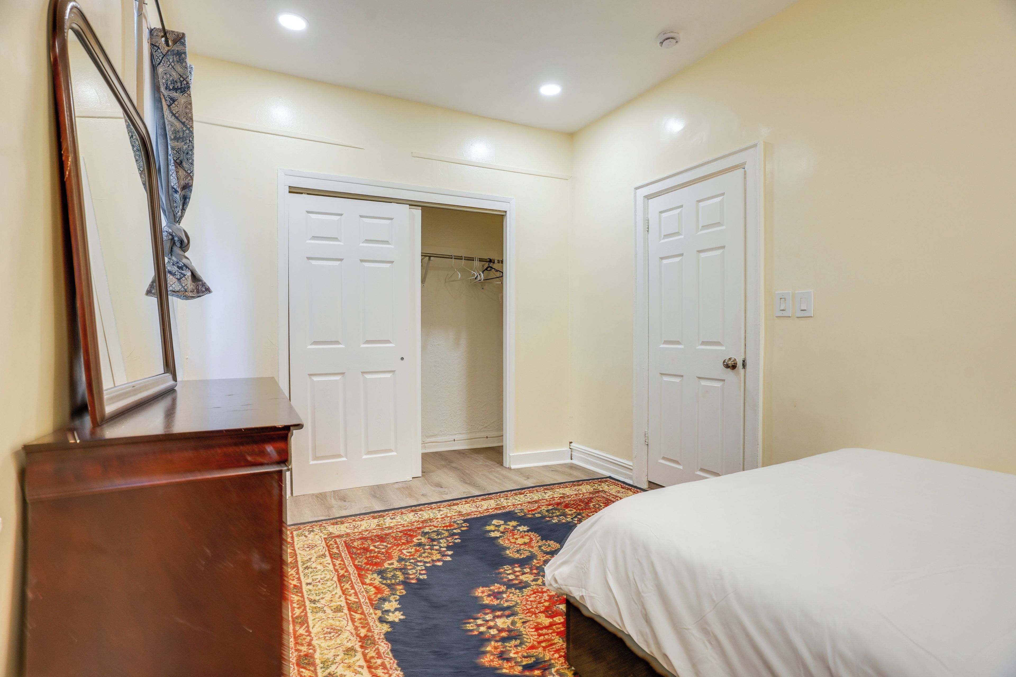 A bedroom with a bed, a dresser, a mirror, and a walk-in closet.