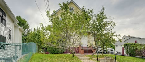 A residential property with a paved driveway leading to a front door, surrounded by a green lawn and a chain-link fence.