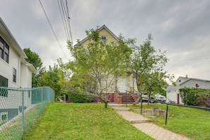 A residential property with a paved driveway leading to a front door, surrounded by a green lawn and a chain-link fence. - Near Shops & Transit to Nyc! Yonkers Apt (Yonkers)