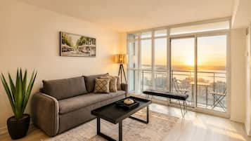 Una sala de estar moderna con un sofá, una mesa de centro y vistas de un paisaje urbano a través de grandes ventanales.