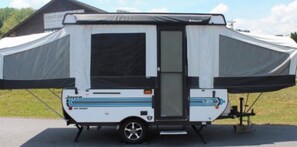 A Jayco RV with a large awning, a door, and wheels. - Jayco Light Pop Up Trailer (Ajax)
