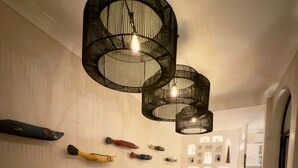 Uma sala de jantar com uma mesa comprida posta para várias pessoas, rodeada por cadeiras de vime, sob um moderno candelabro preto.