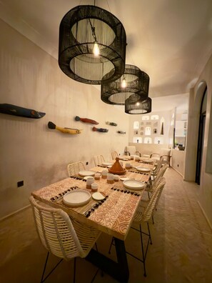 A dining area with a long table set for multiple people, surrounded by wicker chairs, under a modern black chandelier. - Vrbo Property (Marrakech)