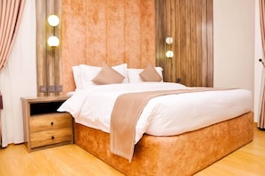 Una cama bien hecha con ropa de cama blanca y beige, un cabecero de madera y lámparas de noche.