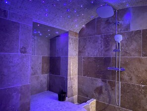 Un baño con ducha, paredes de azulejos e iluminación empotrada en el techo.