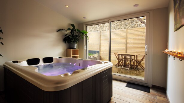 A modern bathroom with a freestanding hot tub, a potted plant, and a wooden table and chairs outside. - La maison du moulin - gîte et spa privatif avec hammam traditionnel et jacuzzi (Damblainville)