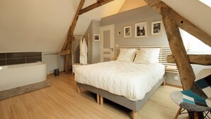 A bedroom with a sloped ceiling, a bed with white bedding, a wooden chair, and a small bedside table. - La maison du moulin - gîte et spa privatif avec hammam traditionnel et jacuzzi (Damblainville)