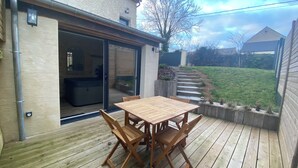A wooden deck with a table and chairs, a sliding glass door, and a grassy backyard. - La maison du moulin - gîte et spa privatif avec hammam traditionnel et jacuzzi (Damblainville)