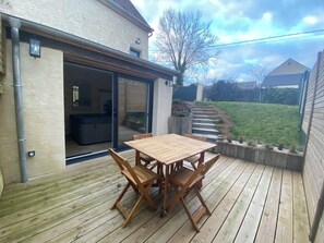 Una terraza de madera con una mesa y sillas, un ventanal corredero y un jardín con césped.