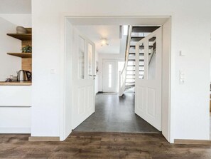 Ein Flur mit einer Treppe, die zu einer zweiten Etage führt, weiße Wände und ein dunkler Holzboden.