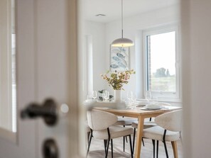A dining area with a round table set for four, a hanging pendant light, and a window with a view of the outdoors. - Holiday Home With 3 Bedrooms (Krummhoern)