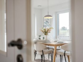 Un comedor con una mesa redonda dispuesta para cuatro, una lámpara colgante y un ventanal con vistas al exterior.
