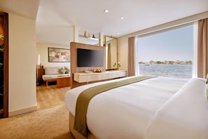 A hotel room with a large bed, a TV, a seating area, and a view of the sea. - MS Royal Serenade (Luxor)