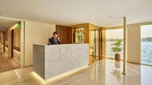 A hotel reception area with a marble counter, a receptionist, and a view of the water. - MS Royal Serenade (Luxor)