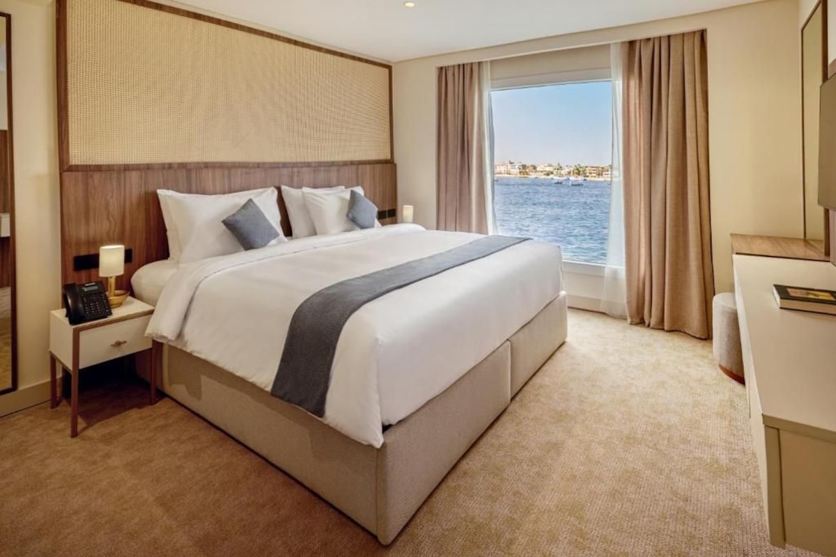 Habitación de hotel con una cama grande, teléfono junto a la cama, mesita de noche y vista al mar.