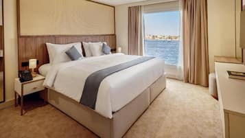 A hotel room with a large bed, a bedside telephone, a nightstand, and a view of the sea.
