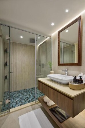Un baño moderno con cabina de ducha de vidrio, lavamanos blanco y mueble de tocador de madera.