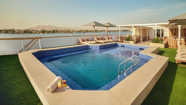 A rooftop pool with a view of a body of water and mountains, surrounded by lounge chairs and umbrellas. - MS Royal Serenade (Luxor)
