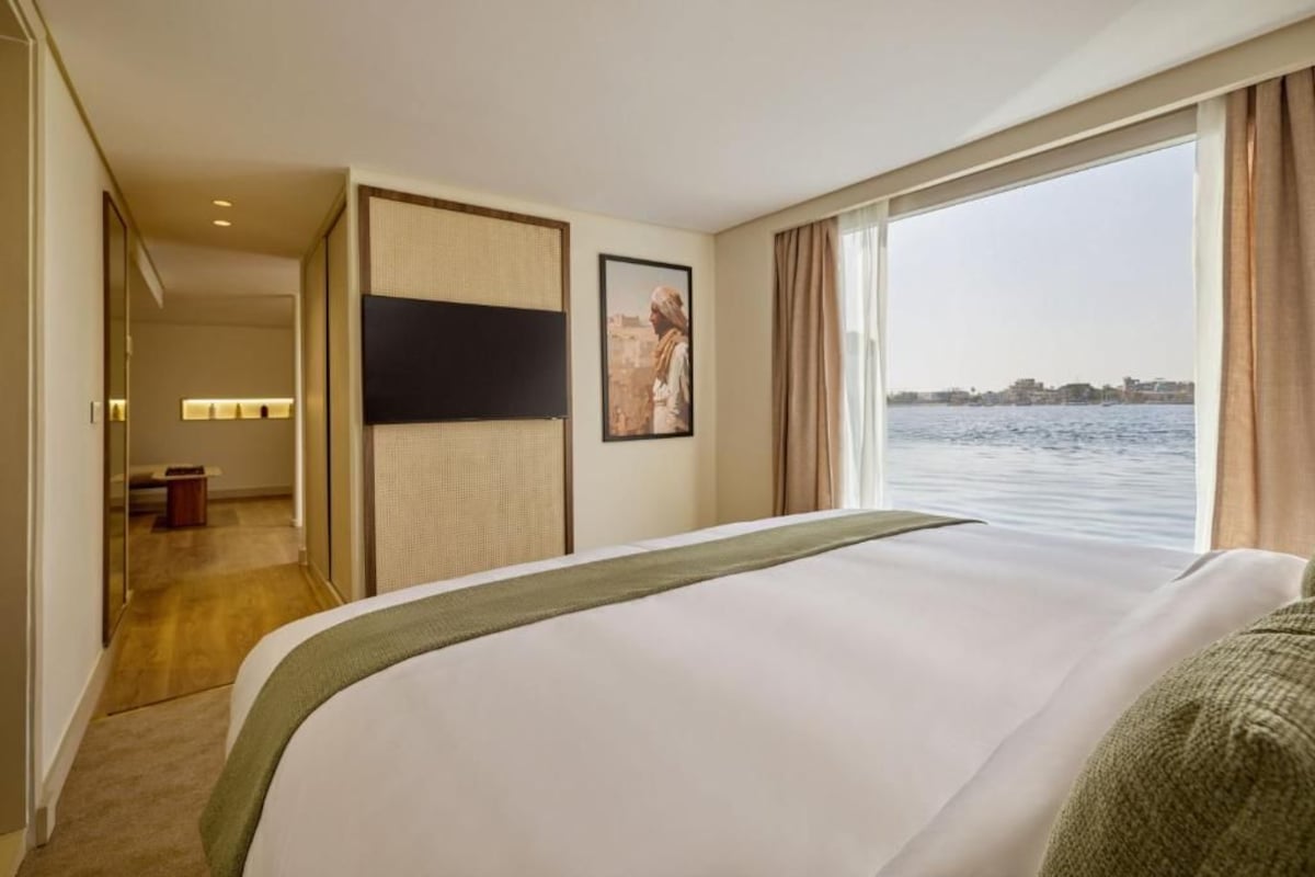 Habitación de hotel con una cama, vistas al agua y un paisaje urbano al fondo.