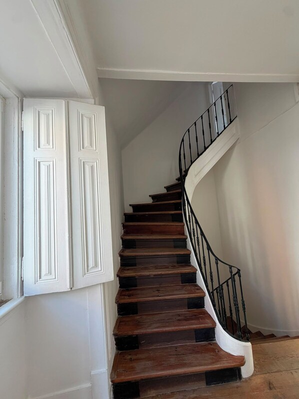 Un escalier en colimaçon avec des marches en bois et des rampes noires, menant à l’étage supérieur.
