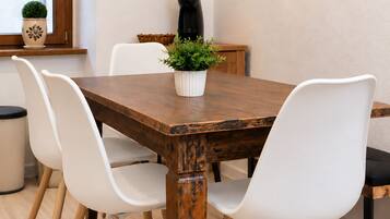 Een eetgedeelte met een houten tafel, witte stoelen, een potplant en een koffieapparaat.