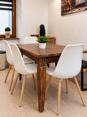 Een eetgedeelte met een houten tafel, witte stoelen, een potplant en een koffieapparaat.