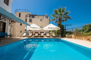 Una piscina amb gandules i ombrel·les, envoltada d'un edifici amb un balcó.