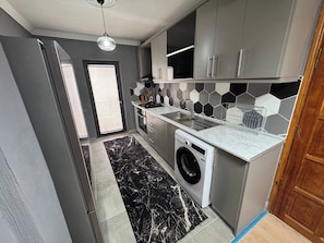 Una cocina moderna con armarios grises, un salpicadero de azulejos blanco y negro, una lavadora y una alfombra con estampado de mármol.