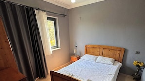 Un dormitorio con una cama de madera, una mesita de noche, una lámpara y una ventana con cortinas.