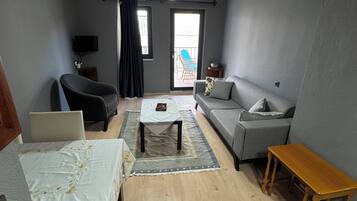 Ein Wohnzimmer mit einer Couch, einem kleinen Tisch, einem Couchtisch, einem Fernseher und einer Balkontür.